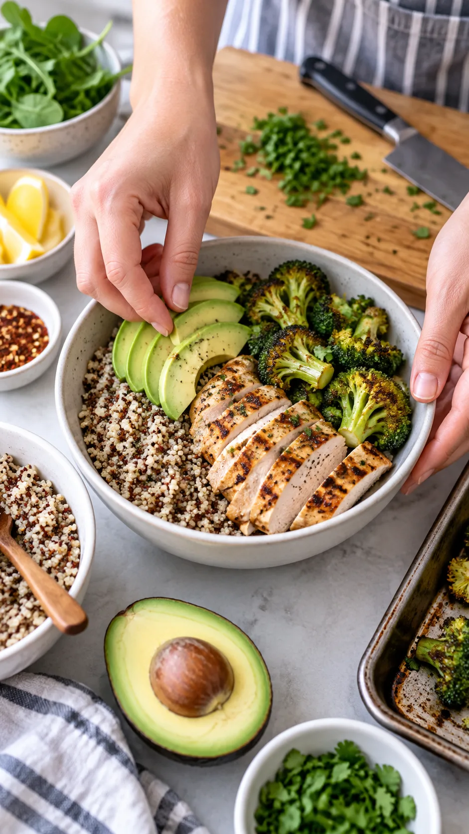 Close-up of hands assembling a meal prep bowl with quinoa, sliced grilled chicken, roasted broccoli and avocado, ingredients arranged in bowls around a wooden cutting board, bright natural lighting