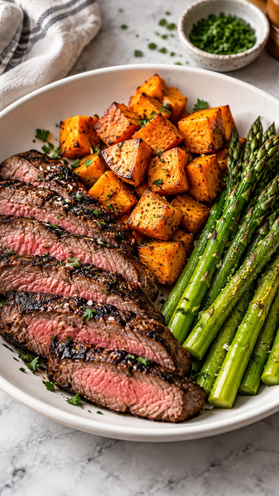 The Female Bulking Meal Plan That Actually Builds Muscle Without the Bloat 4 A delicious, aesthetic fitness dinner bowl featuring grilled flank steak slices, cubed roasted sweet potatoes, and tender steamed asparagus on a matte white plate.